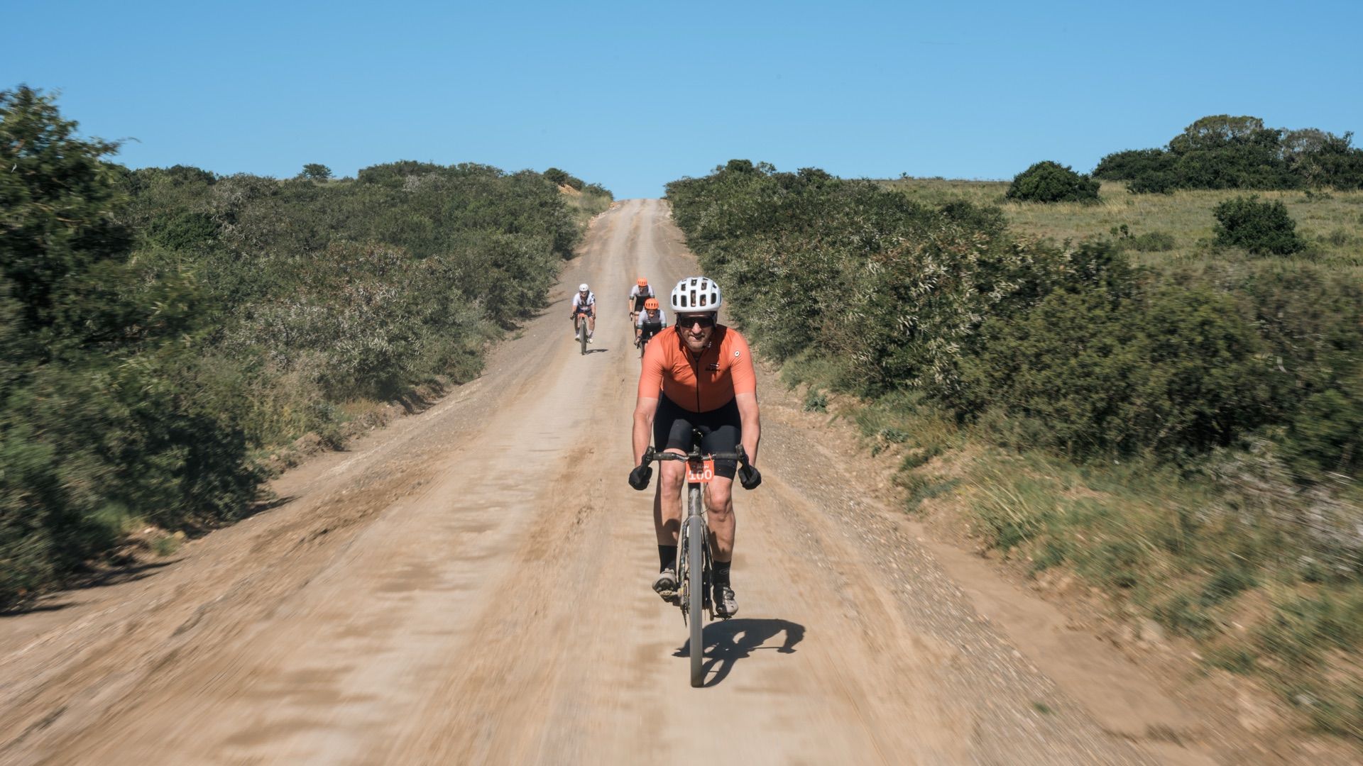 A rider on a fast, straight gravel road through green bush