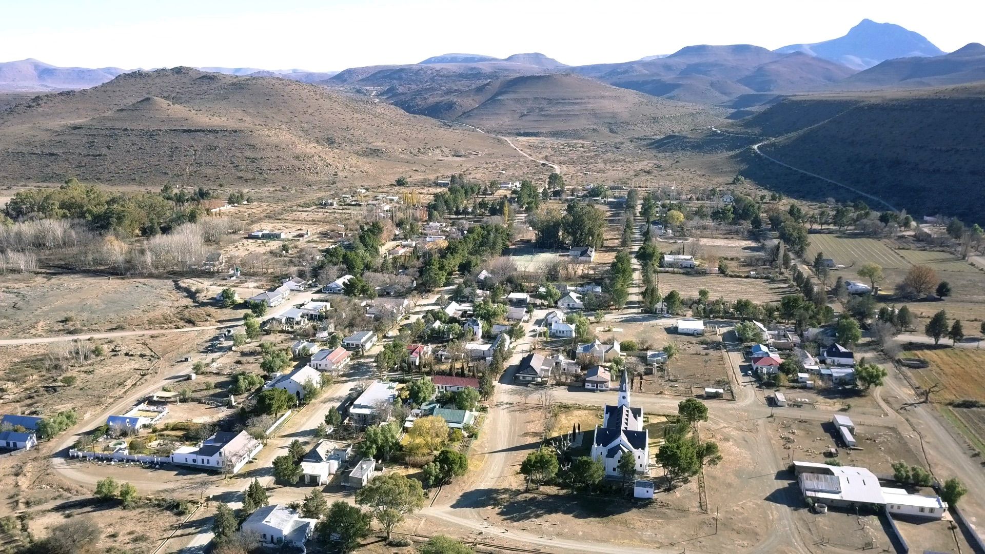 Nieu-Bethesda from the air: a small grid of streets and trees in a valley below the mountains