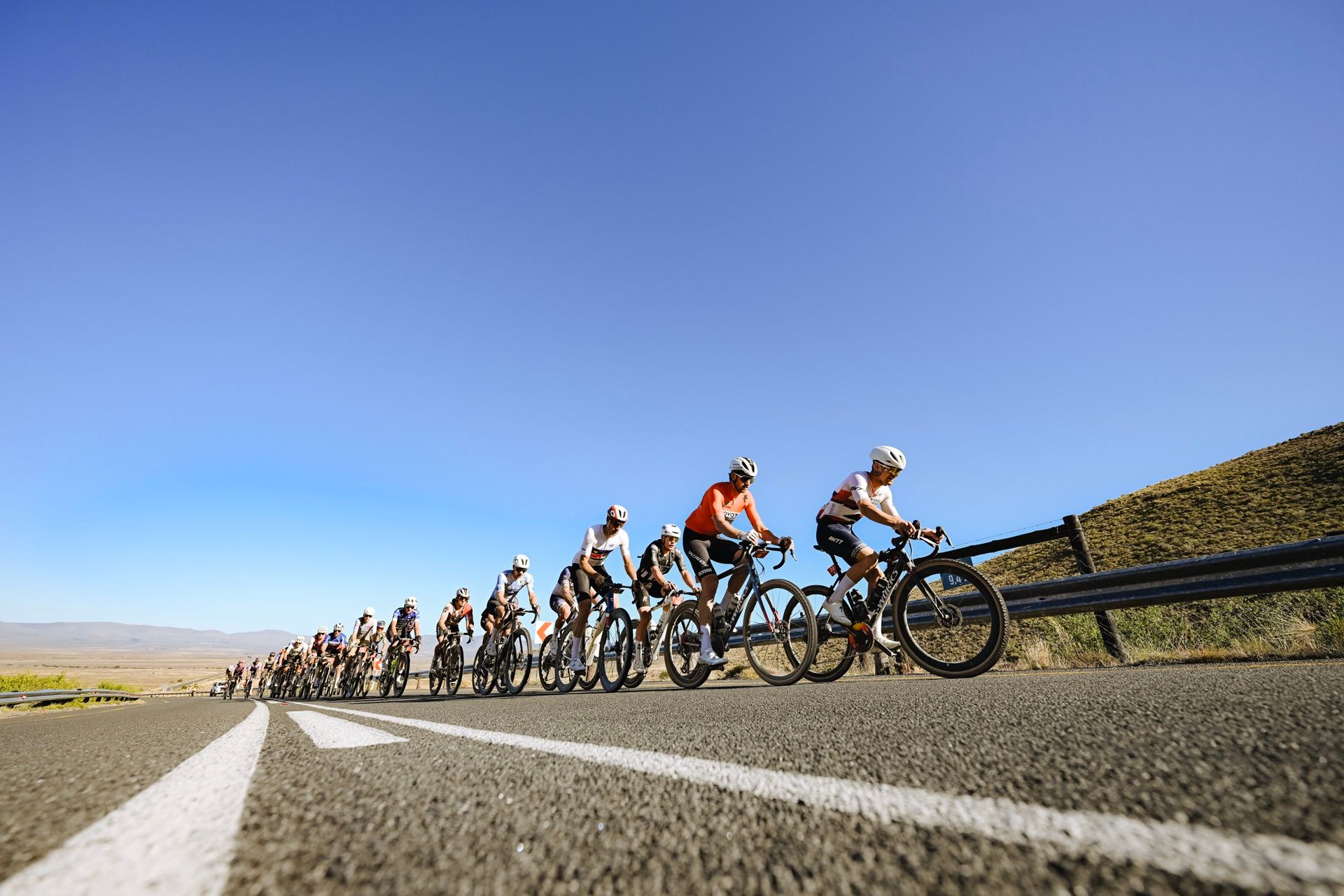 A long paceline of riders on a tarred road