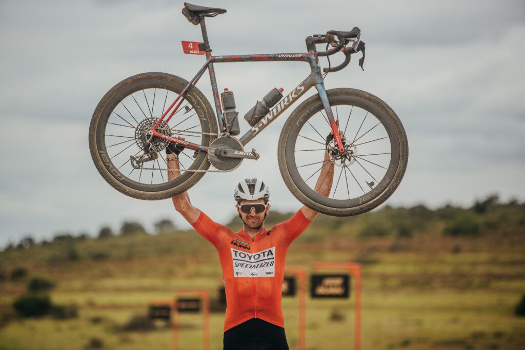 Matthew Beers lifts his bike above his head at the finish of the final stage