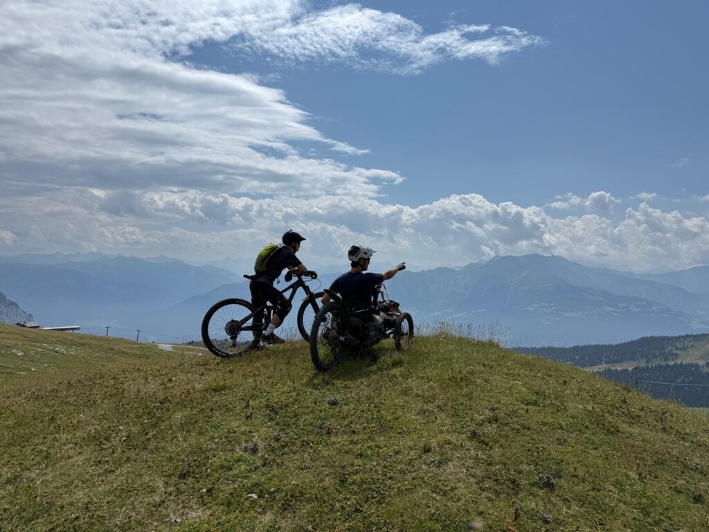 A rider on a Bowhead and a mountain biker looking out over the Swiss Alps from a grassy ridge