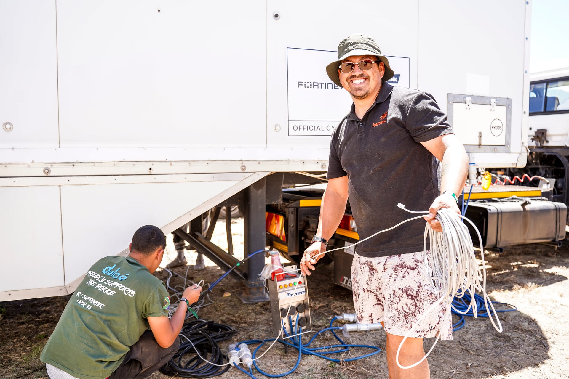 Two crew members connecting network cables beside a technology trailer in a Burn Camp