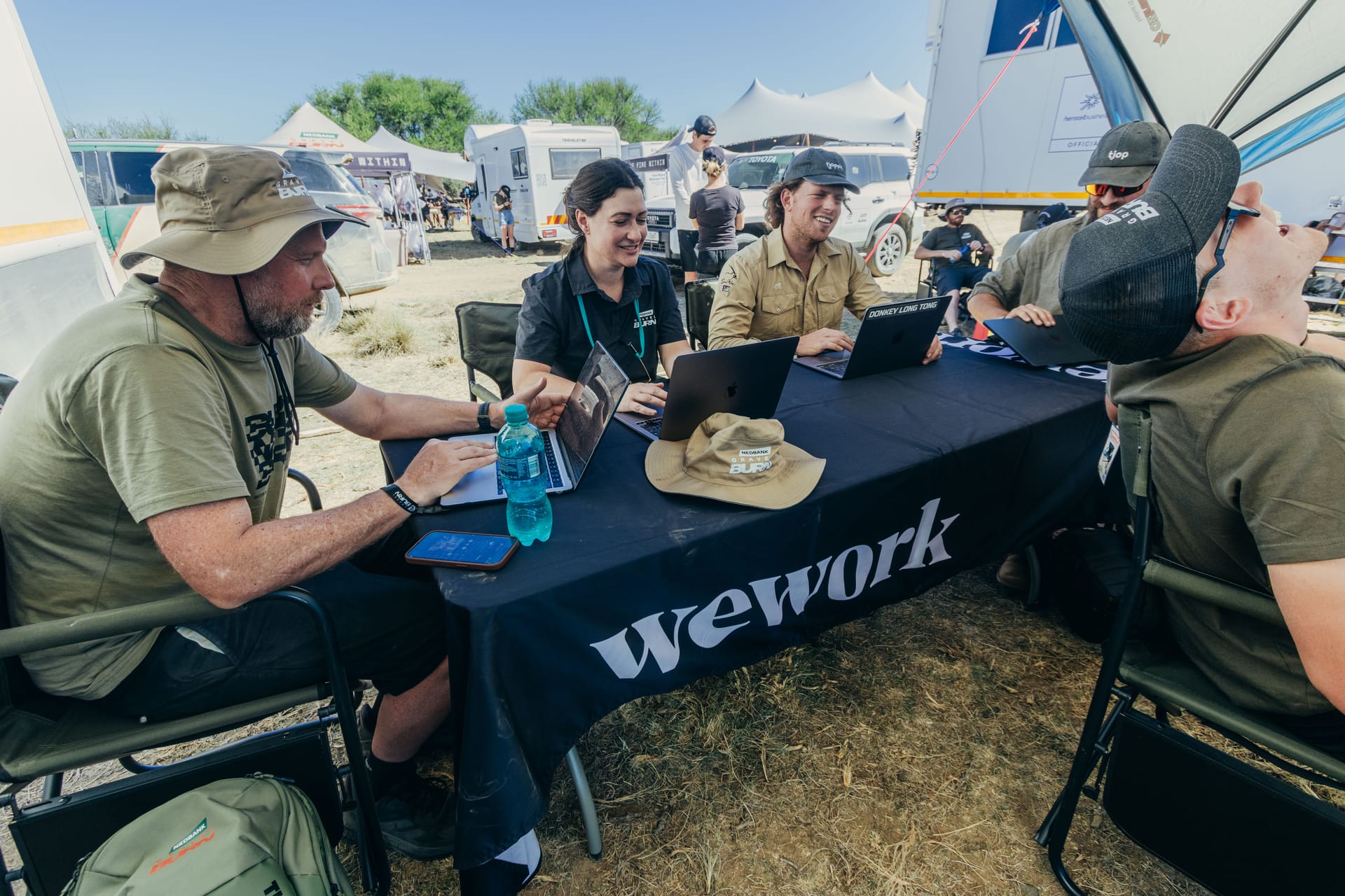Riders and crew working on laptops at a table in the Burn Camp’s WeWork area